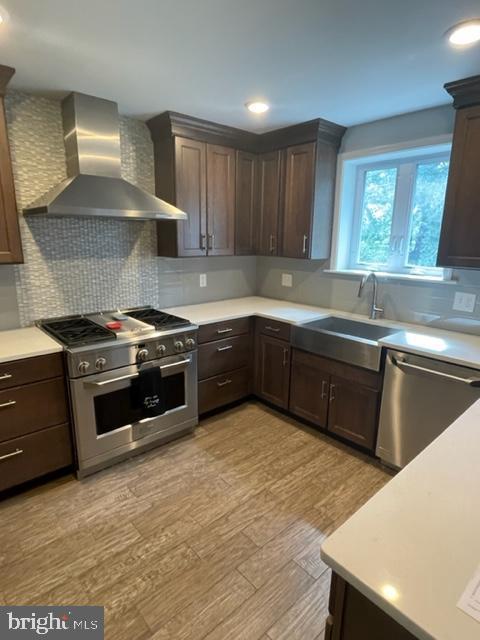 2632 Lenape Rd, Philadelphia, PA 19131 - kitchen featuring wall chimney exhaust hood, stainless steel appliances, light wood-style flooring, dark brown cabinets, and recessed lighting