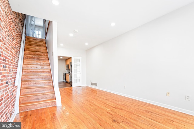 1622 E Clement St, Baltimore, MD 21230 - unfurnished living room with light wood finished floors, stairs, recessed lighting, baseboards, and brick wall