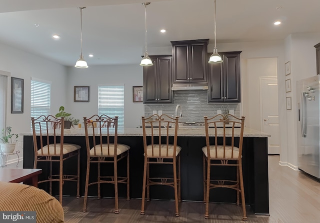 8716 Windon Ct, Waldorf, MD 20603 - kitchen featuring stainless steel fridge, tasteful backsplash, light wood finished floors, under cabinet range hood, and light stone counters