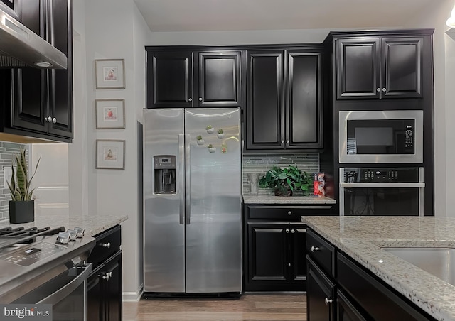 8716 Windon Ct, Waldorf, MD 20603 - kitchen featuring appliances with stainless steel finishes, dark cabinetry, under cabinet range hood, light wood finished floors, and light stone counters