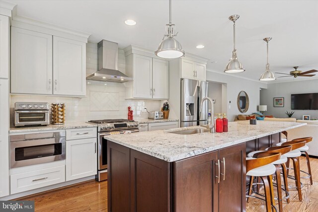 237 Trianon Ln, Villanova, PA 19085 - kitchen featuring stainless steel appliances, wall chimney range hood, a sink, open floor plan, and light wood-type flooring