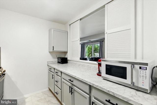 9272 Adelphi Unit 103, Hyattsville, MD 20783 - kitchen with white microwave, light marble finish floors, baseboards, gray cabinetry, and light stone counters