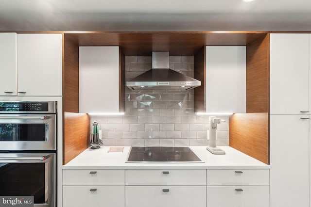 137 Sutton Rd, Ardmore, PA 19003 - kitchen with double oven, wall chimney exhaust hood, black electric cooktop, tasteful backsplash, and white cabinetry