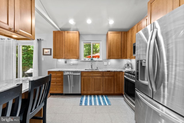 5209 Stonington Dr, Fairfax, VA 22032 - kitchen featuring appliances with stainless steel finishes, decorative backsplash, light stone counters, brown cabinetry, and a sink