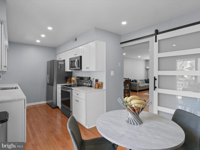 12215 Wye Oak Commons Cir Unit 66, Burke, VA 22015 - kitchen with stainless steel appliances, a barn door, a sink, white cabinets, and light wood-style flooring