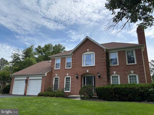 9802 Days Farm Dr, Vienna, VA 22182 - colonial house featuring a chimney, asphalt driveway, a front yard, an attached garage, and brick siding