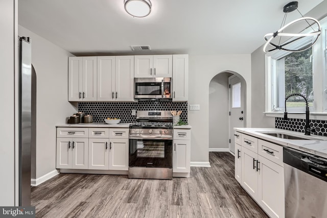 6505 Corkley Rd, Baltimore, MD 21237 - kitchen featuring stainless steel appliances, a sink, arched walkways, backsplash, and light wood-style floors