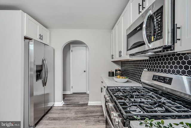 6505 Corkley Rd, Baltimore, MD 21237 - kitchen featuring stainless steel appliances, arched walkways, wood finished floors, tasteful backsplash, and white cabinetry