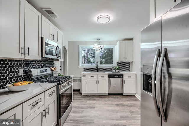 6505 Corkley Rd, Baltimore, MD 21237 - kitchen featuring stainless steel appliances, a sink, radiator, light wood-style floors, and decorative backsplash