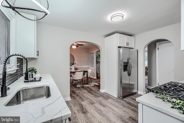 6505 Corkley Rd, Baltimore, MD 21237 - kitchen with stainless steel fridge, a sink, arched walkways, and white cabinets