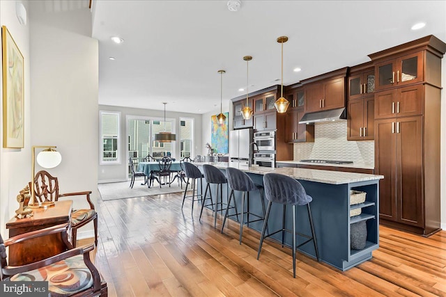 368 Star Tavern Ln, West Chester, PA 19382 - kitchen featuring under cabinet range hood, light wood-style floors, appliances with stainless steel finishes, a kitchen bar, and open shelves