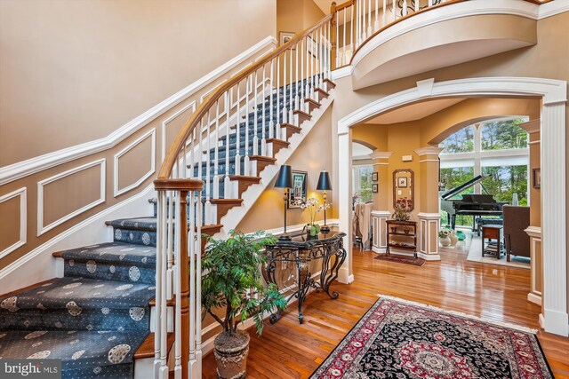 18403 Rim Rock Cir, Leesburg, VA 20176 - stairs featuring ornate columns, arched walkways, wood finished floors, a high ceiling, and a decorative wall