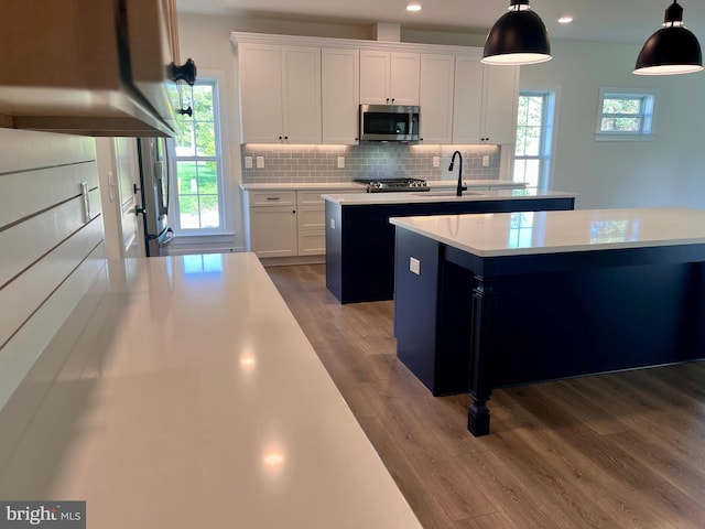 34232 Brenner Ln, Lewes, DE 19958 - kitchen featuring stainless steel microwave, an island with sink, a sink, wood finished floors, and decorative backsplash