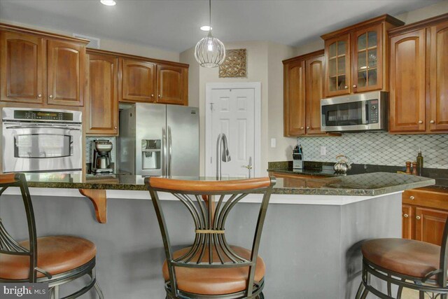 11516 Mystic Rock Ln N, Waynesboro, PA 17268 - kitchen featuring appliances with stainless steel finishes, a kitchen breakfast bar, backsplash, glass insert cabinets, and brown cabinetry