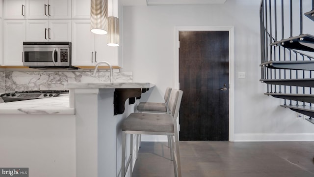 1323 Clifton St NW Unit 34, Washington, DC 20009 - kitchen featuring stainless steel microwave, white cabinetry, light stone countertops, and decorative backsplash