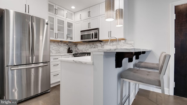 1323 Clifton St NW Unit 34, Washington, DC 20009 - kitchen featuring stainless steel appliances, light stone countertops, decorative backsplash, white cabinetry, and a breakfast bar