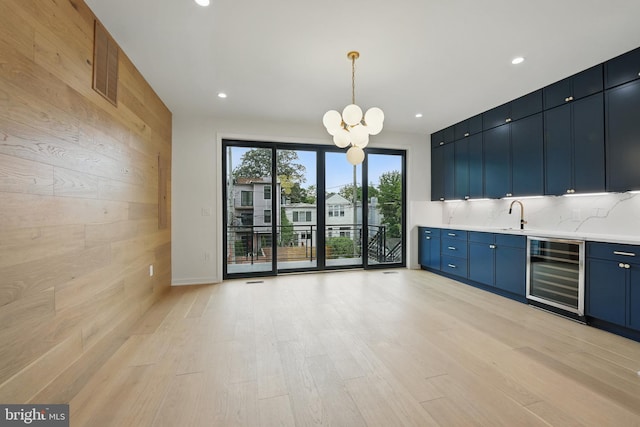 3802 T St NW, Washington, DC 20007 - unfurnished living room with beverage cooler, a chandelier, wood walls, bar with sink, and light wood-type flooring