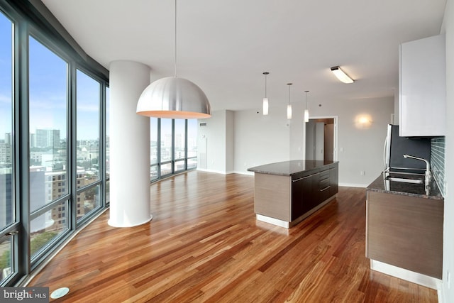 2101 Market St Unit 902, Philadelphia, PA 19103 - kitchen featuring a sink, a kitchen island, light wood finished floors, dark stone counters, and hanging light fixtures