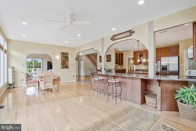 927 Brick Manor Cir, Silver Spring, MD 20905 - kitchen featuring appliances with stainless steel finishes, arched walkways, a kitchen bar, brown cabinetry, and light stone countertops