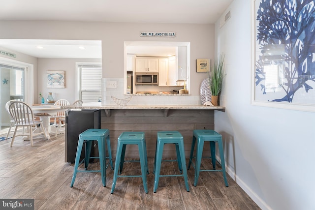 183 Jamestown Rd Unit 10, Ocean City, MD 21842 - kitchen featuring stainless steel microwave, a kitchen breakfast bar, wood finished floors, decorative backsplash, and recessed lighting