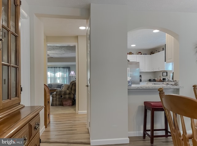 6165 Hawthorne Rd, La Plata, MD 20646 - kitchen with freestanding refrigerator, arched walkways, light wood-type flooring, a kitchen bar, and white cabinetry