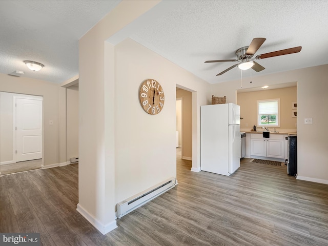 111 S Buchannan St, Ranson, WV 25438 - unfurnished living room with a baseboard heating unit, a textured ceiling, ceiling fan, wood finished floors, and baseboards