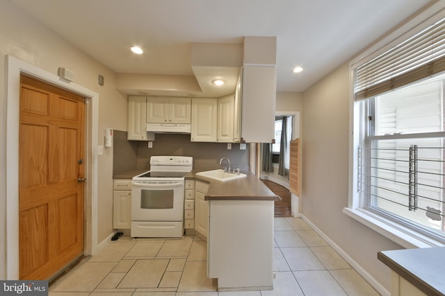 5331 Race St, Philadelphia, PA 19139 - kitchen with white electric stove, under cabinet range hood, a sink, light tile patterned floors, and white cabinets