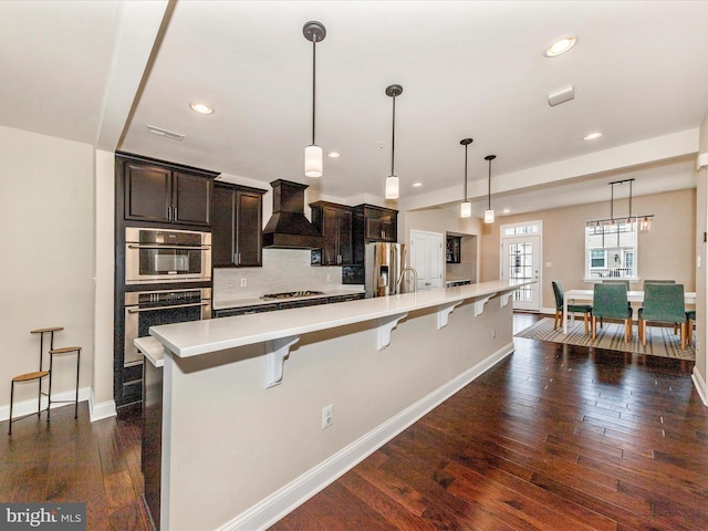 7114 Proclamation Pl, Frederick, MD 21703 - kitchen featuring premium range hood, stainless steel appliances, light countertops, a breakfast bar area, and dark wood-type flooring