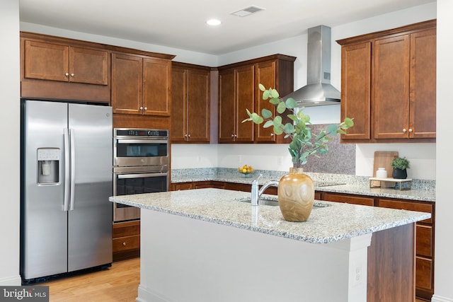 118 Milkweed Dr, Lake Frederick, VA 22630 - kitchen featuring appliances with stainless steel finishes, wall chimney range hood, an island with sink, light stone countertops, and light wood-style floors