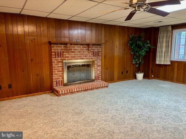 132 Popodickon Dr, Boyertown, PA 19512 - unfurnished living room with a ceiling fan, a paneled ceiling, wooden walls, carpet flooring, and a fireplace