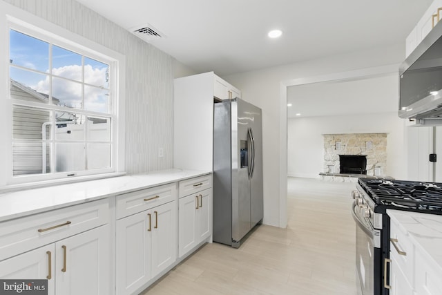 3835 Dresher Rd, Bensalem, PA 19020 - kitchen featuring appliances with stainless steel finishes, white cabinetry, light stone counters, a stone fireplace, and open floor plan