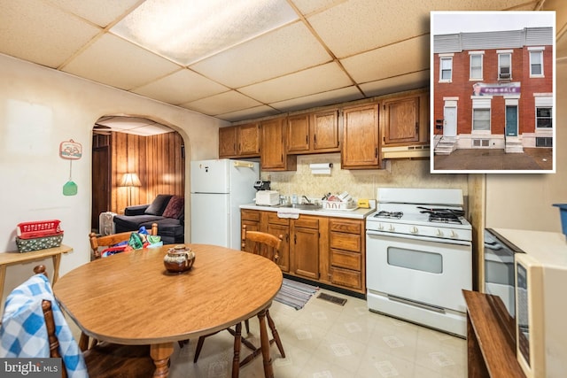 113 N Highland Ave, Baltimore, MD 21224 - kitchen with white appliances, arched walkways, a drop ceiling, under cabinet range hood, and brown cabinets