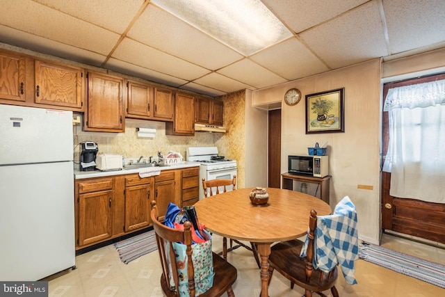 113 N Highland Ave, Baltimore, MD 21224 - kitchen featuring white appliances, a sink, brown cabinetry, under cabinet range hood, and a drop ceiling
