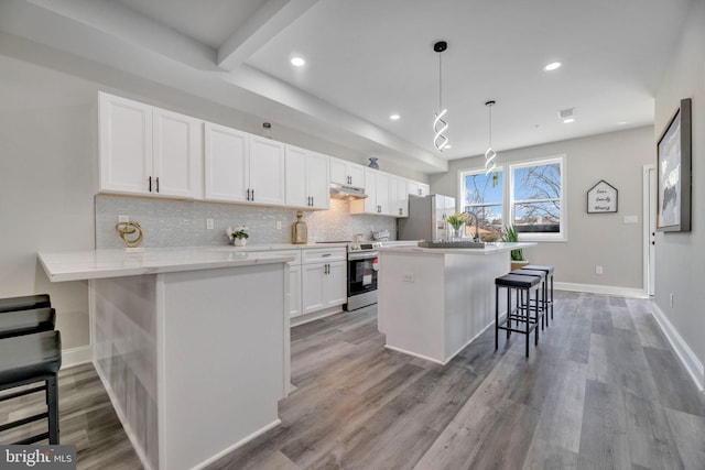 1121 48th Pl NE, Washington, DC 20019 - kitchen with stainless steel appliances, a kitchen breakfast bar, under cabinet range hood, white cabinetry, and recessed lighting