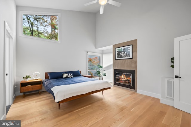 2201 Burgee Ct, Reston, VA 20191 - bedroom with light wood-style floors, a fireplace, baseboards, a towering ceiling, and a ceiling fan
