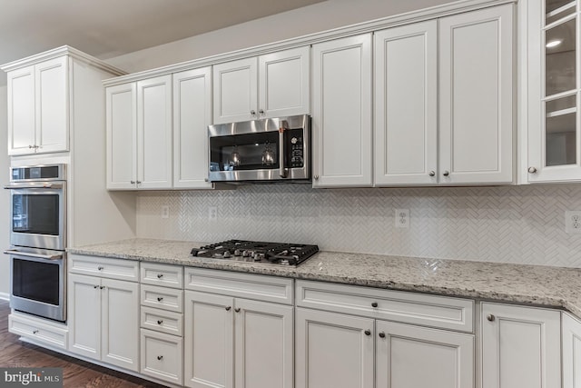 33841 Joel Ln, Lewes, DE 19958 - kitchen featuring stainless steel appliances, white cabinetry, tasteful backsplash, glass insert cabinets, and light stone countertops