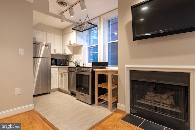 1731 Willard St NW Unit 102, Washington, DC 20009 - kitchen with appliances with stainless steel finishes, white cabinetry, light wood-type flooring, a fireplace with flush hearth, and baseboards