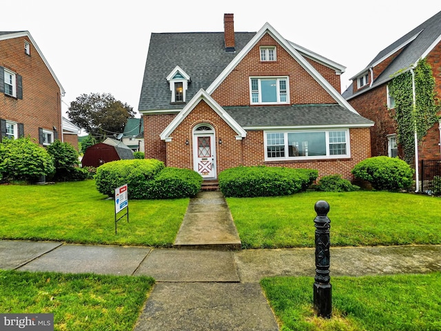 1216 23rd Ave, Altoona, PA 16601 - tudor home featuring roof with shingles, a chimney, a front lawn, and brick siding