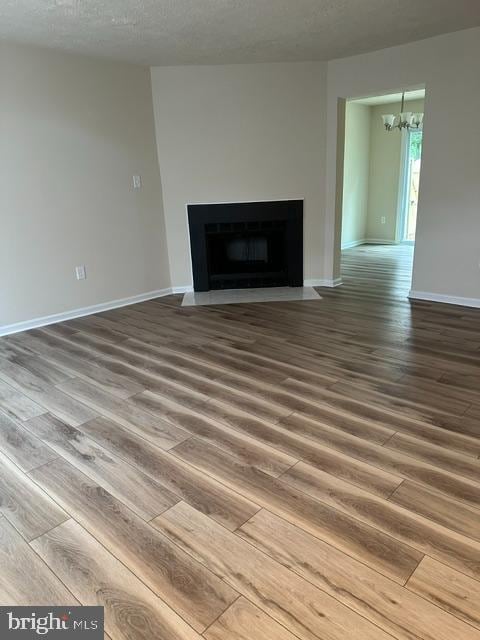 4321 Drake Ct, Waldorf, MD 20603 - unfurnished living room featuring wood finished floors, a chandelier, a fireplace with flush hearth, baseboards, and a textured ceiling