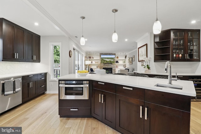 1367 Cedar Ave, Annapolis, MD 21403 - kitchen featuring stainless steel appliances, a sink, a stone fireplace, dark brown cabinetry, and light wood-style flooring