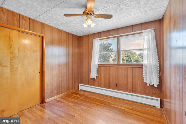 176 Morris Ave, Sewell, NJ 08080 - unfurnished room featuring a baseboard heating unit, wood finished floors, wood walls, ceiling fan, and baseboards