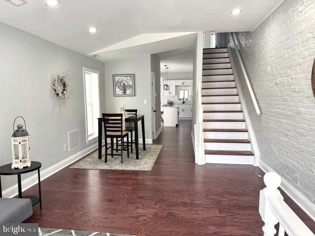 2621 E Monument St, Baltimore, MD 21205 - dining room featuring dark wood-type flooring, stairs, baseboards, brick wall, and recessed lighting