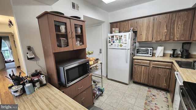 2921 N Leisure World Blvd Unit 418, Silver Spring, MD 20906 - kitchen with freestanding refrigerator, stainless steel microwave, glass insert cabinets, and a textured ceiling