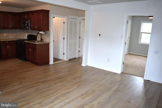 23 Foxglove St, Browns Mills, NJ 08015 - kitchen featuring black range with gas stovetop, stainless steel microwave, light wood finished floors, decorative backsplash, and light stone countertops