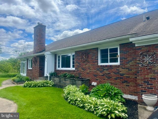 724 E Curtin St, Bellefonte, PA 16823 - view of side of home featuring brick siding, a chimney, a yard, and roof with shingles