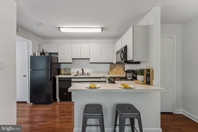 304 Duncan Ave Unit F, Alexandria, VA 22301 - kitchen with black appliances, dark wood-type flooring, a peninsula, light countertops, and a breakfast bar