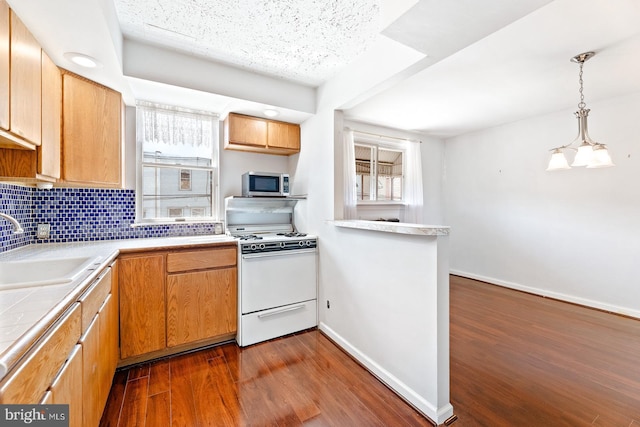7155 Erdrick St, Philadelphia, PA 19135 - kitchen featuring white gas range, stainless steel microwave, a sink, dark wood-style floors, and backsplash