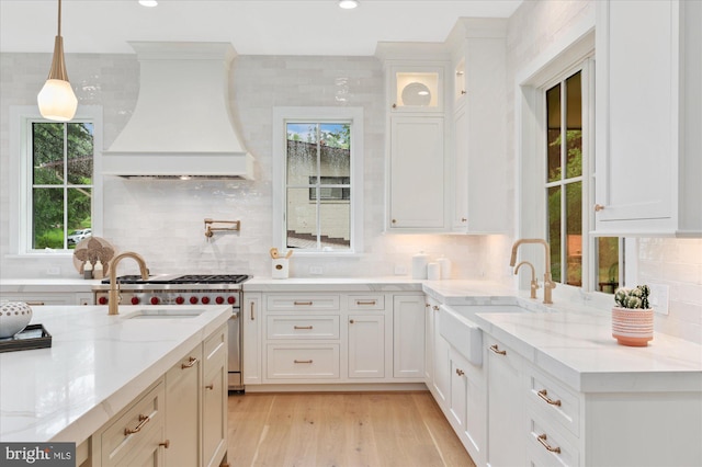 6613 Byrnes Dr, Mclean, VA 22101 - kitchen featuring wall chimney range hood, a sink, white cabinets, tasteful backsplash, and light wood finished floors