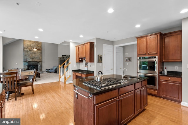 8800 Primula Dr, Laytonsville, MD 20882 - kitchen with stainless steel appliances, a sink, light wood-style flooring, a fireplace, and an island with sink