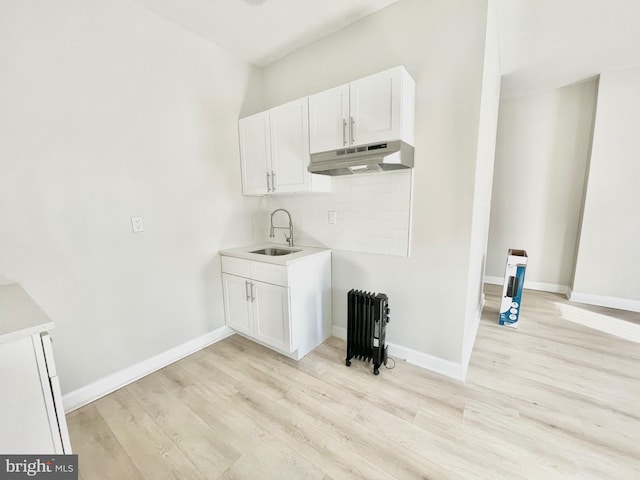 6227 Callowhill St, Philadelphia, PA 19151 - kitchen featuring under cabinet range hood, a sink, light wood-style flooring, decorative backsplash, and radiator heating unit